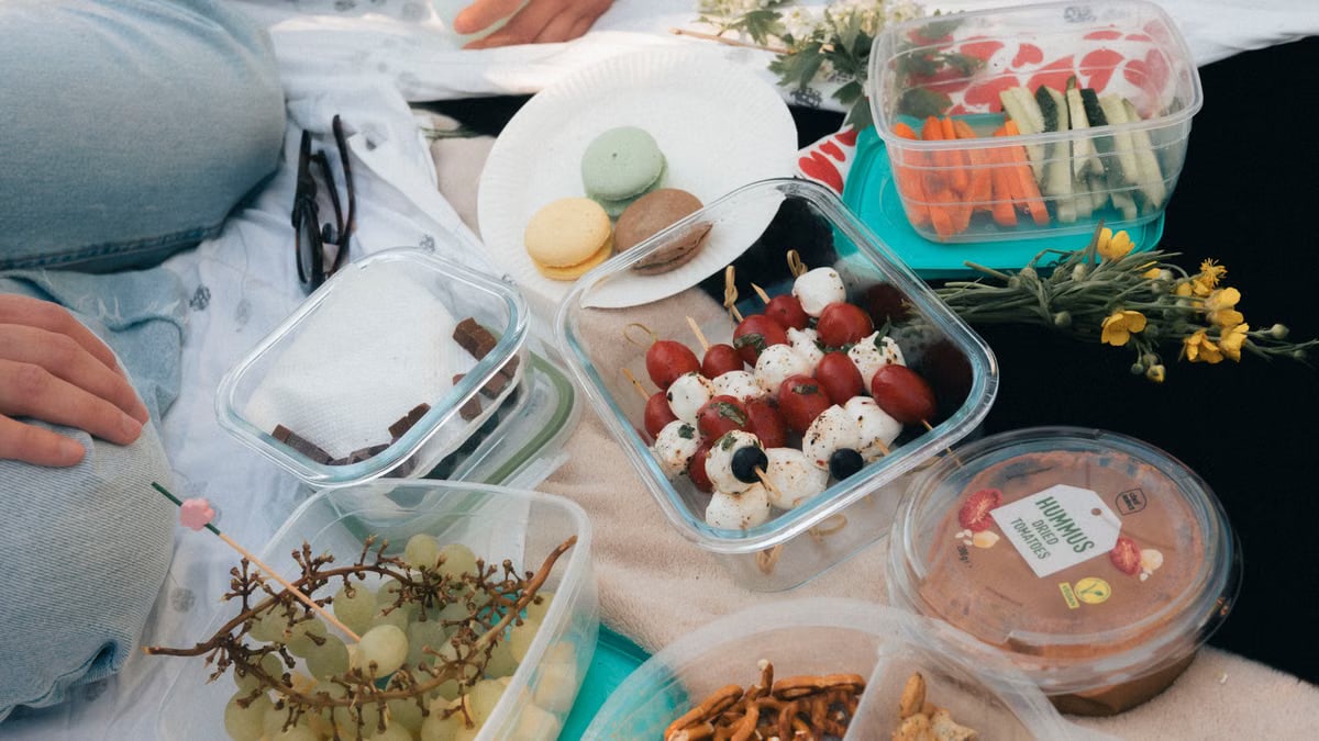 A delightful picnic setup with fresh fruits, vegetables, hummus, and macarons on a sunny day.